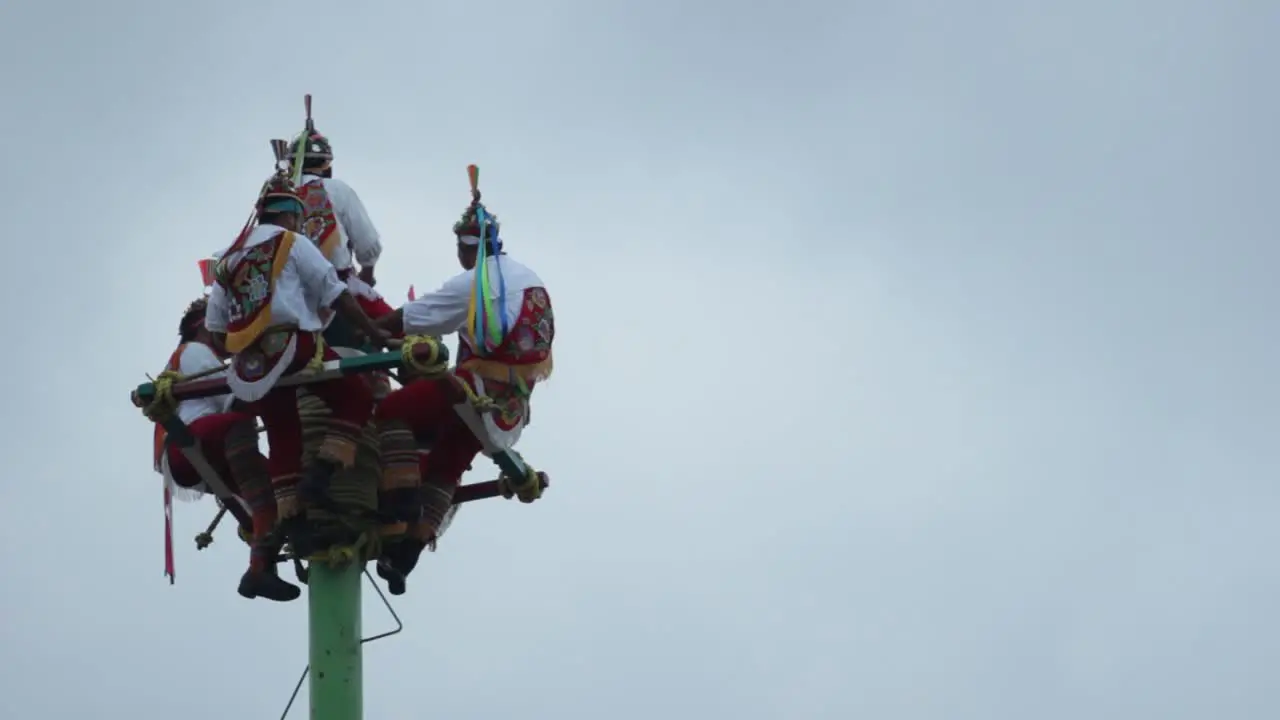 Papantla dancers on the top of the pole playing drums during a cloudy day