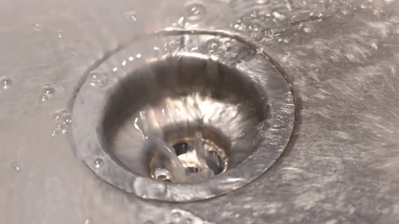 Close up slow motion shot of water draining down a stainless steel sink