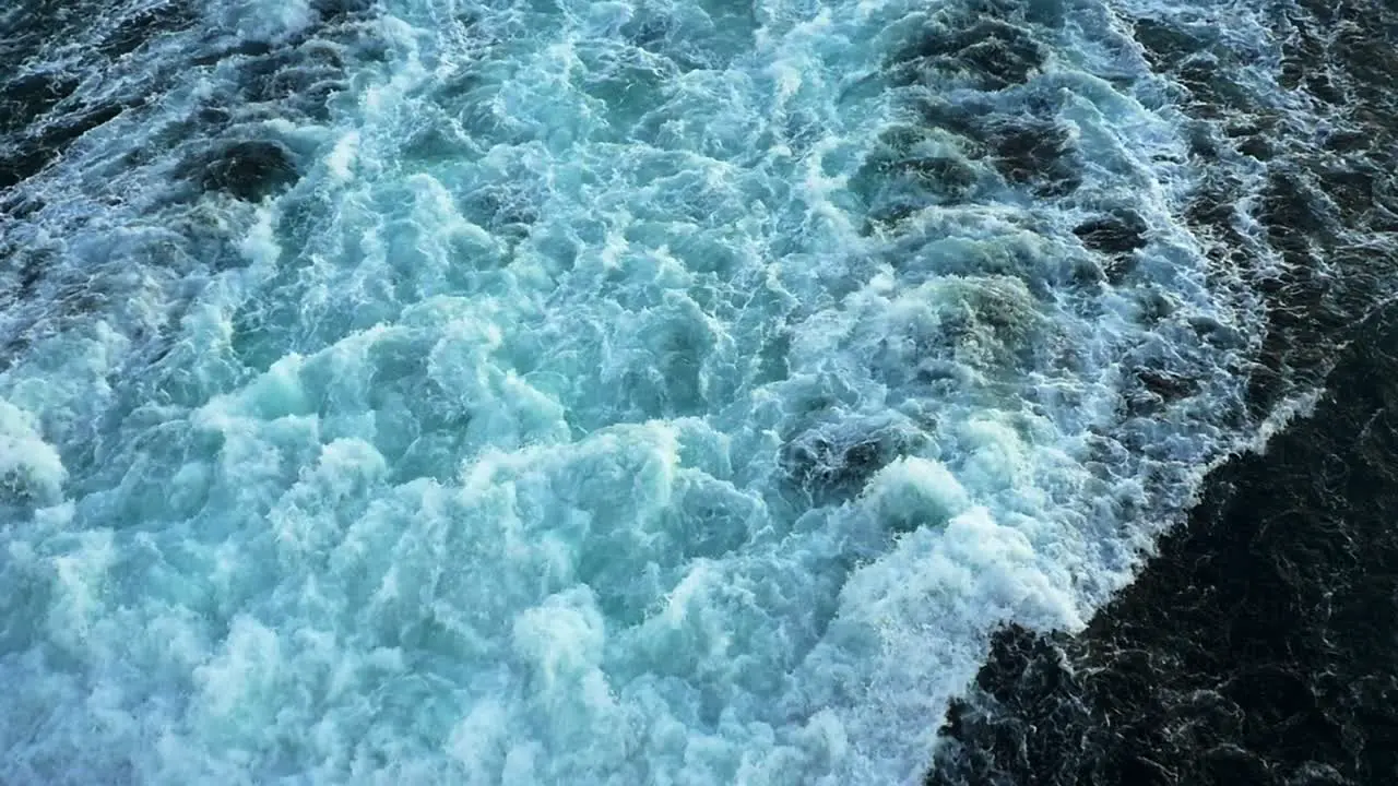 Tilt-up shot of large churning prop wash from the stern of a cruise ship to horizon in slow motion