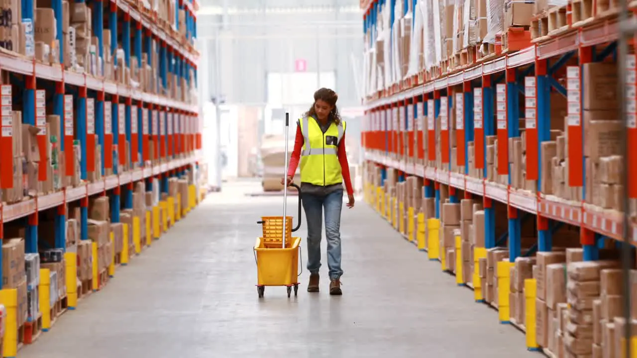 Female warehouse worker walking with mop and bucket