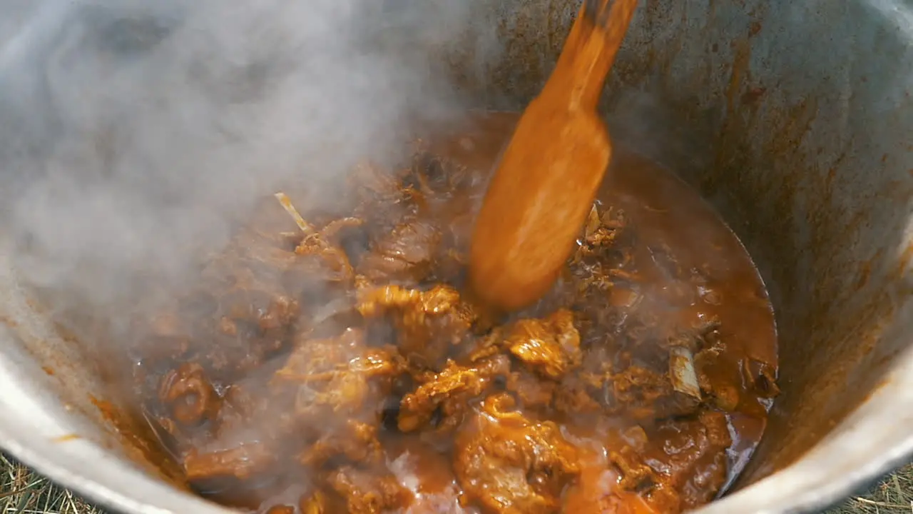 slow motion of cooking lamb stew with wooden spoon in big cauldron