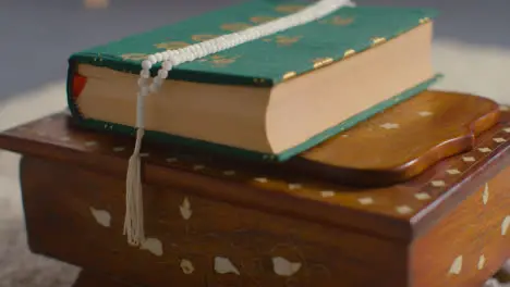 Close Up Of Closed Copy Of The Quran On Stand At Home With Prayer Beads