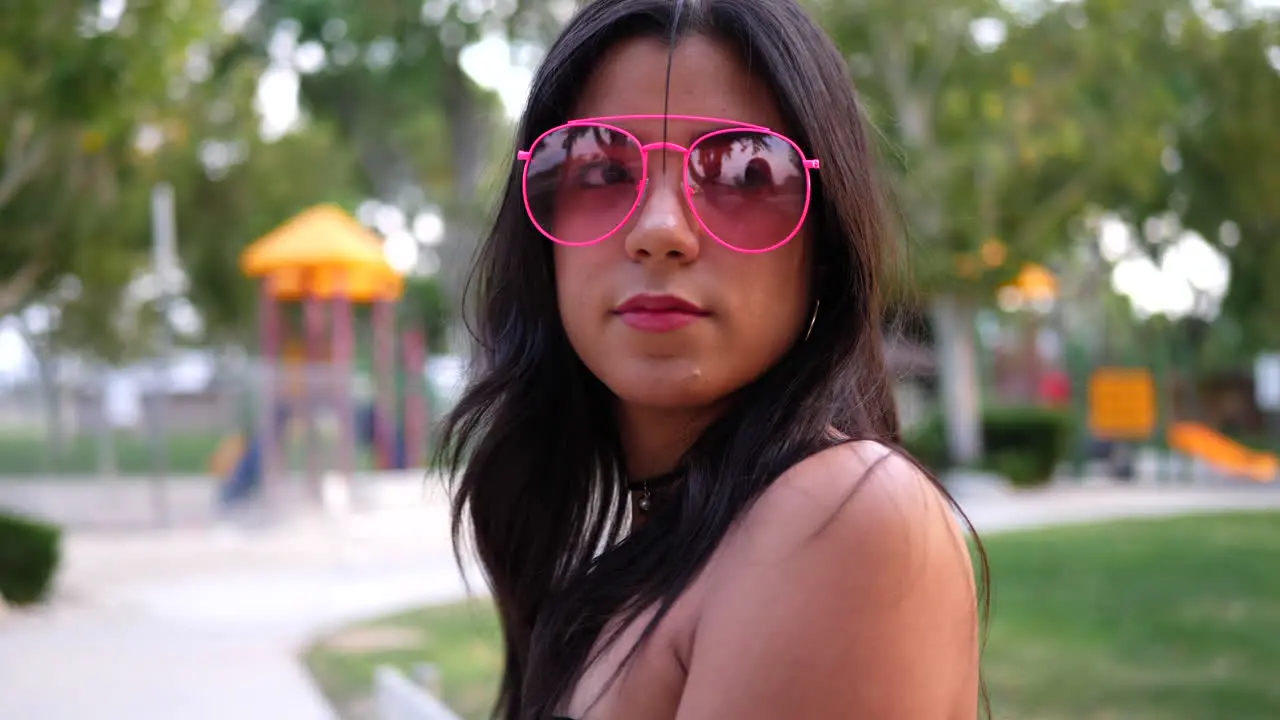 A young woman hipster wearing vintage fashion clothing and retro pink aviator sunglasses in a park playground SLOW MOTION