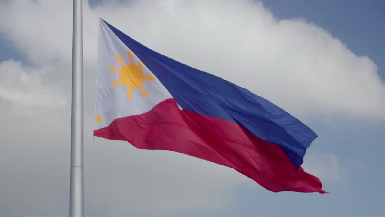 Large Philippine Flag waving in the wind against a partly cloudy sky while on a large flagpole in 4K slow motion