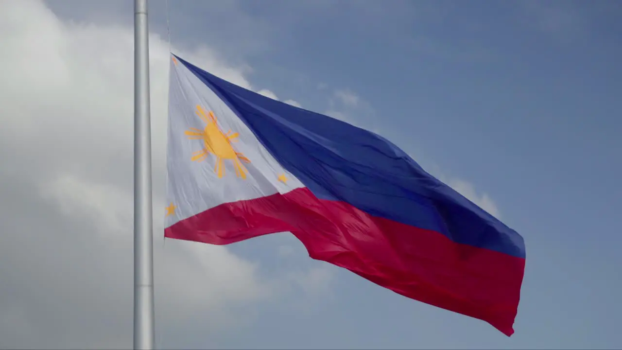 Large Philippine Flag waving in the wind against a partly cloudy sky in 4K slow motion