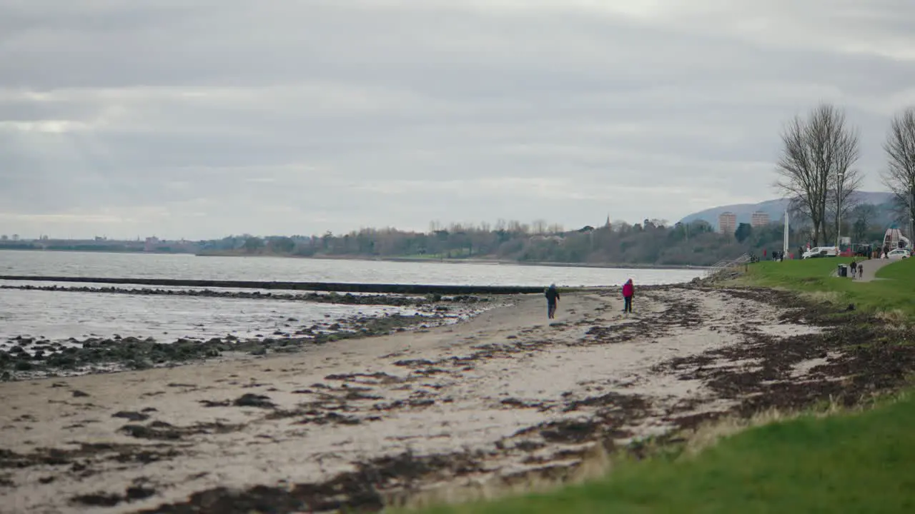 Two people walk on beach on cloudy day slow motion wide shot