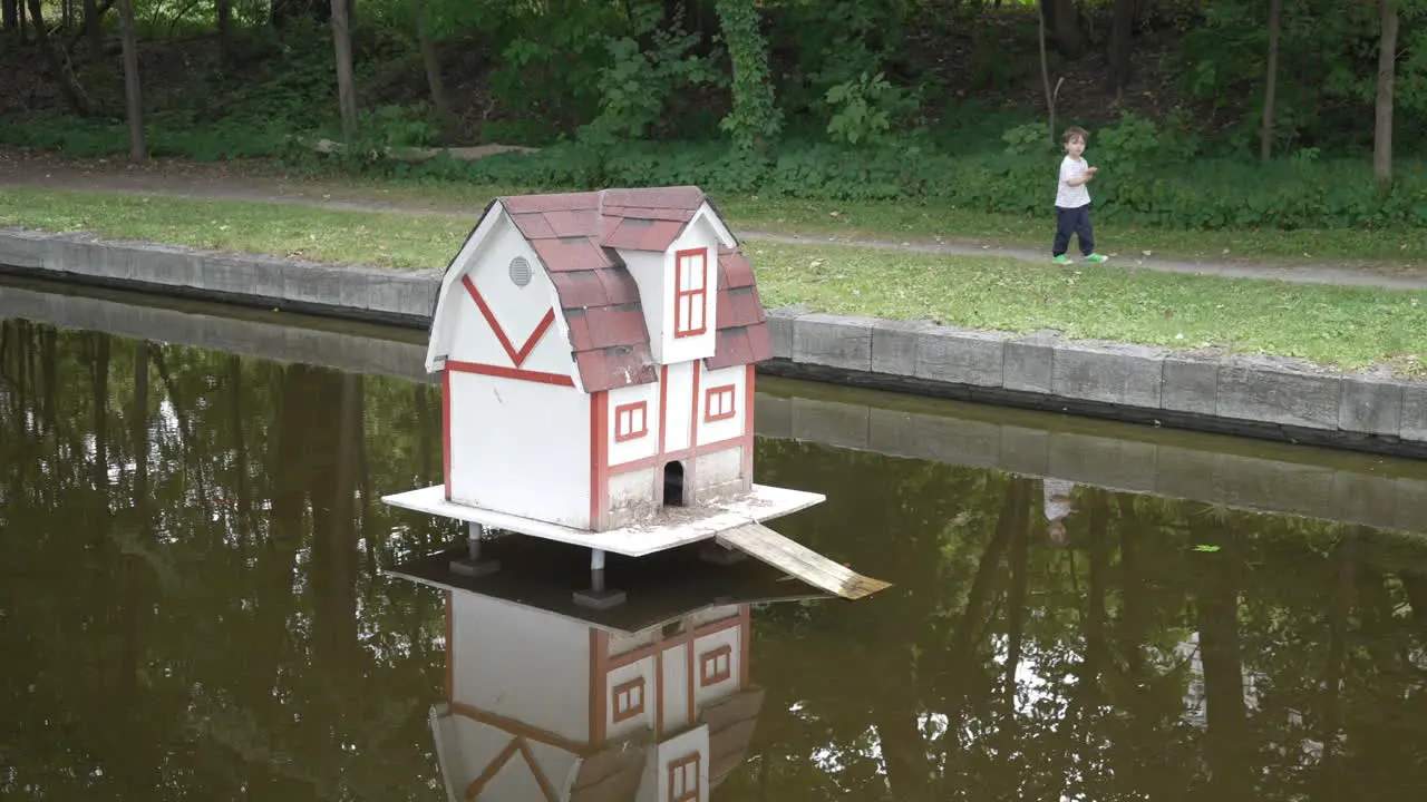 A little boy walks past a duck house at a pond in slow motion