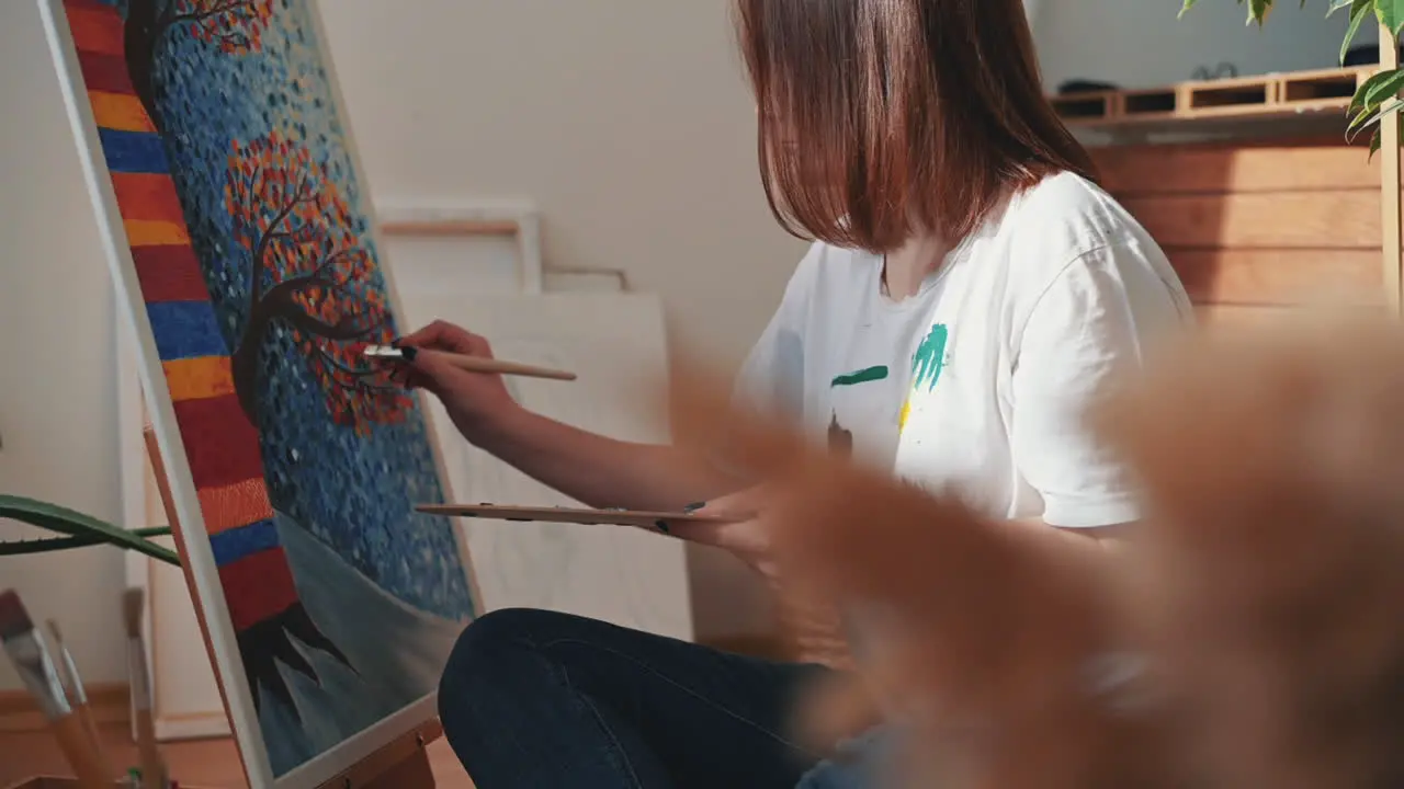 A Red Haired Young Female Artist Mixing Colors On A Painter's Palette And Painting A Canvas