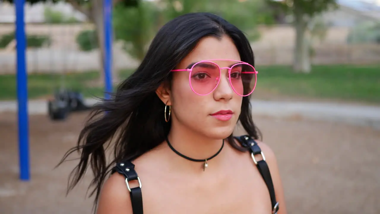 A young hispanic woman hipster wearing vintage fashion clothing and retro pink aviator sunglasses in a park playground