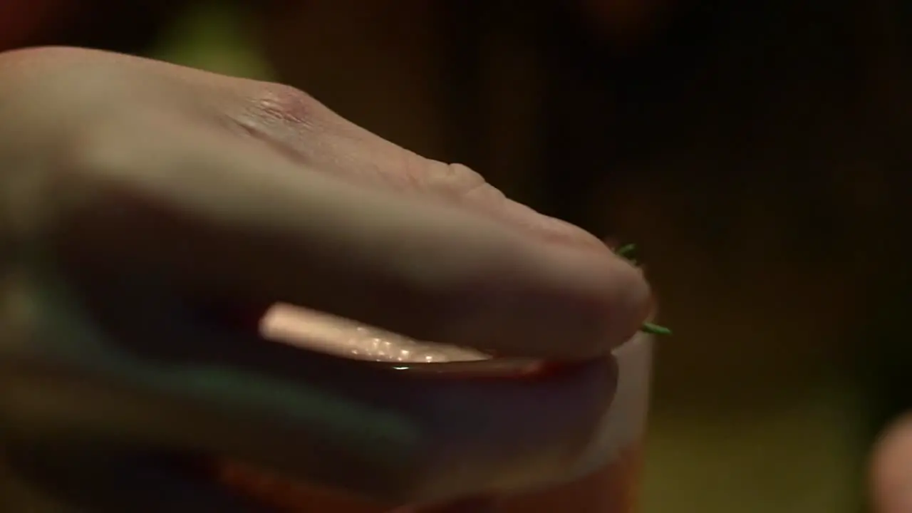 Extreme close up of frothy tropical cocktail being dressed with rosemary leaves filmed in slow motion