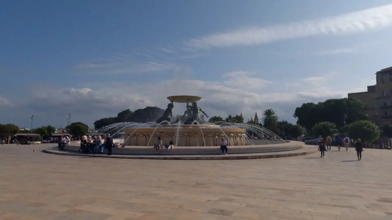 Slow motion shot of tourists walking by the Triton Fountain in Valletta Malta