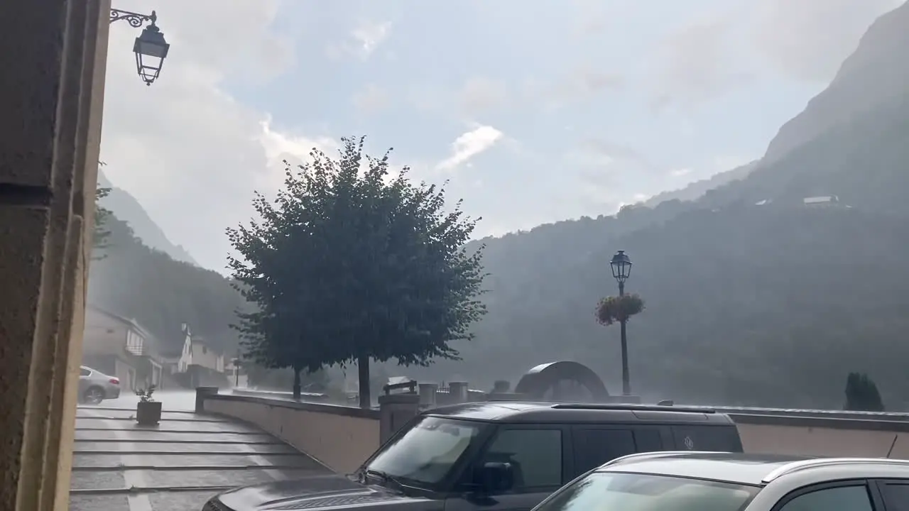 Landscape shot rain and hail hitting cars during the day in the street of gavarnie gedre village in the wild pyrenees mountain national parc with a slow motion