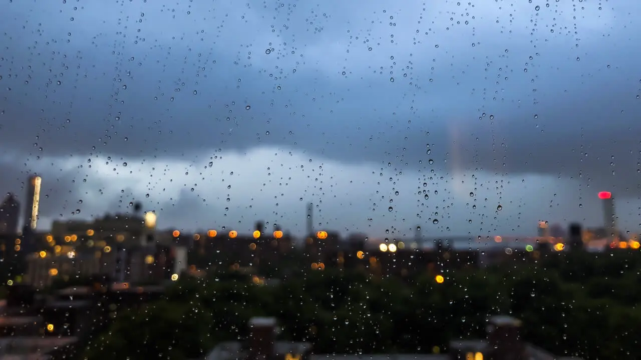 Raindrops gather on windowpane while the evening lights of New York City come up in the background