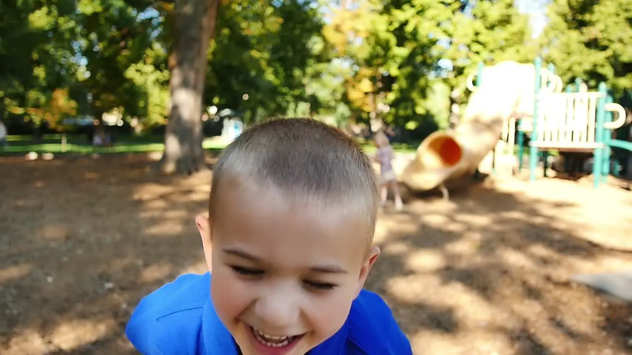 Happy little boy on playground throws his head back and laughs in slow motion