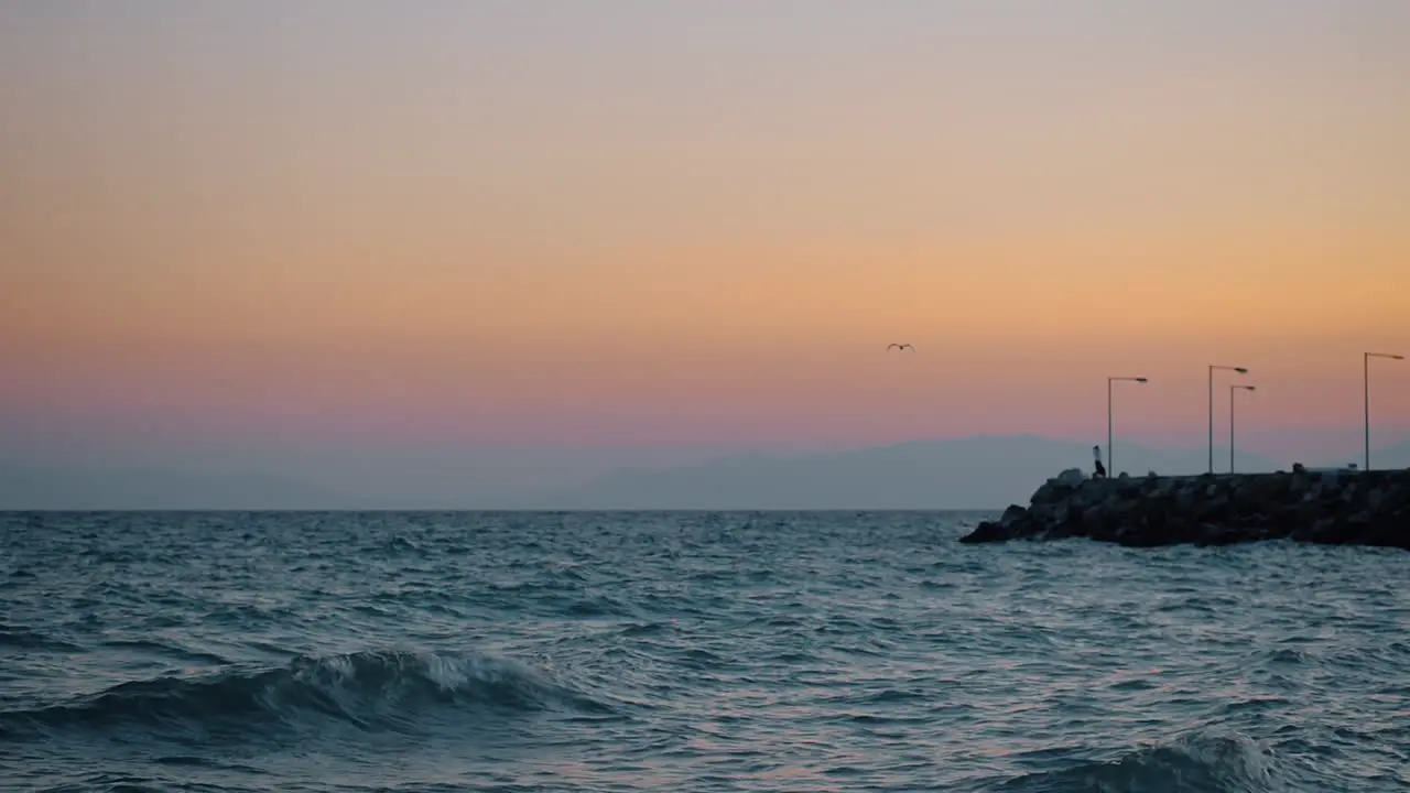 Evening waterscape with wavy sea rocky pier and flying gull