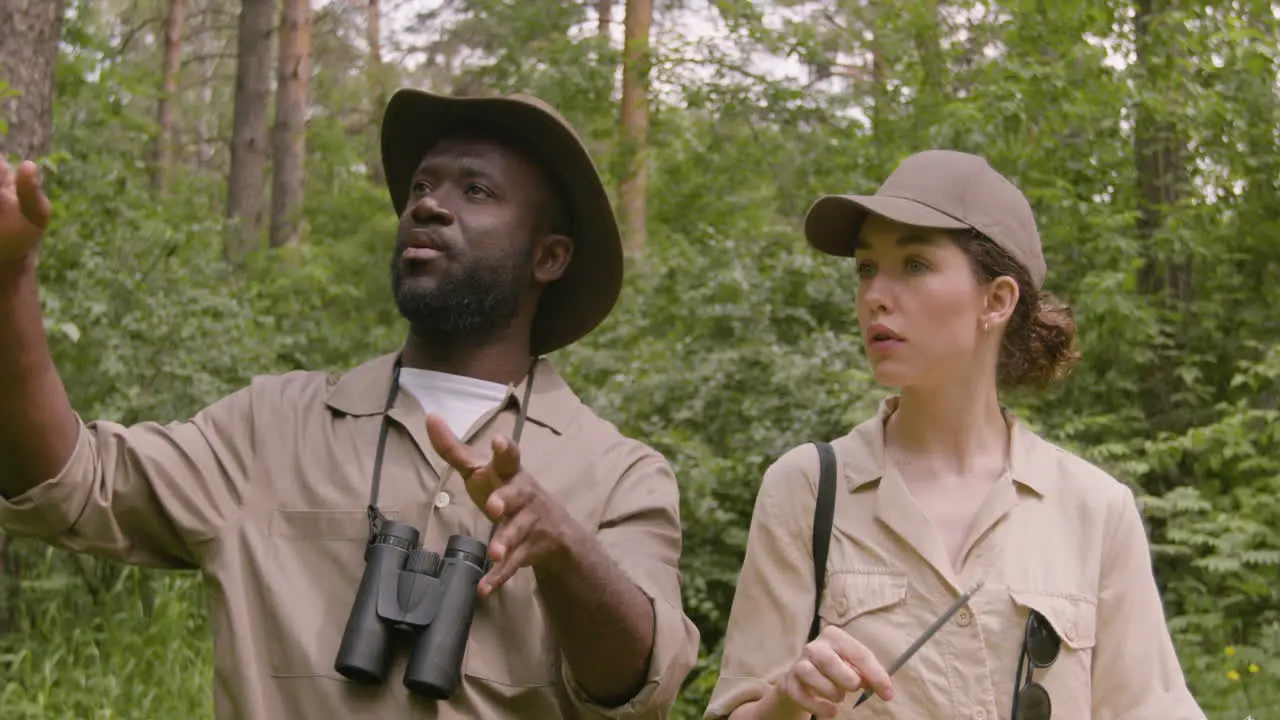 Caucasian and african american forest wardens taking notes and talking while walking in the woods