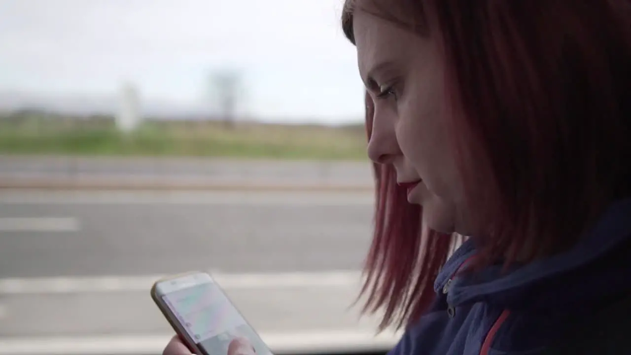 Slow motion close up shot of a girl browsing her smartphone while driving in a vehicle with motion in the background