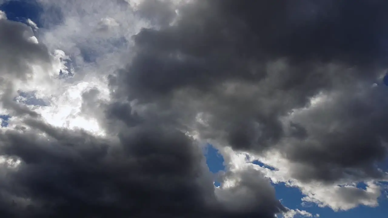 Vibrant Sunlight Hiding Behind Dark Grey Clouds Moving In Blue Sky low angle time lapse