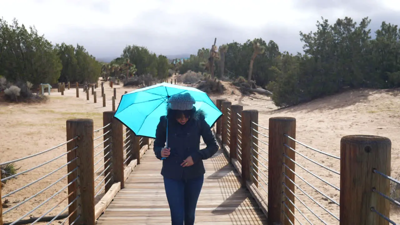 Pretty woman walking across a bridge with a blue rain umbrella with stormy cloudy skies above SLOW MOTION