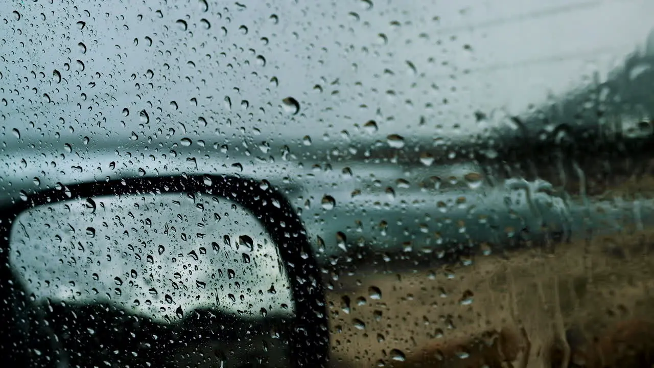 Fat raindrops on car window on rainy day blurry ocean waves in background