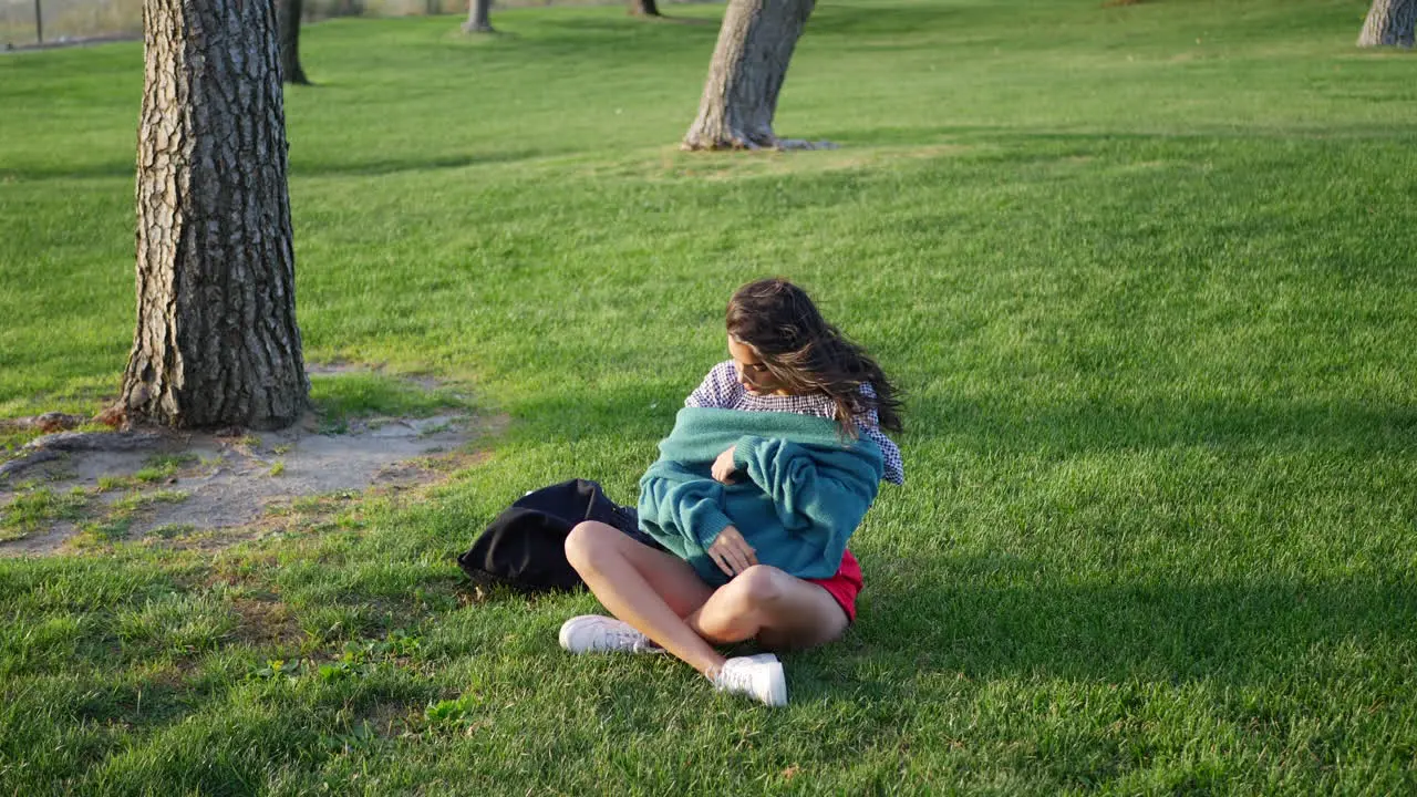 A beautiful young hispanic woman in a park trying to get warm and cozy with her sweater in cold season windy weather