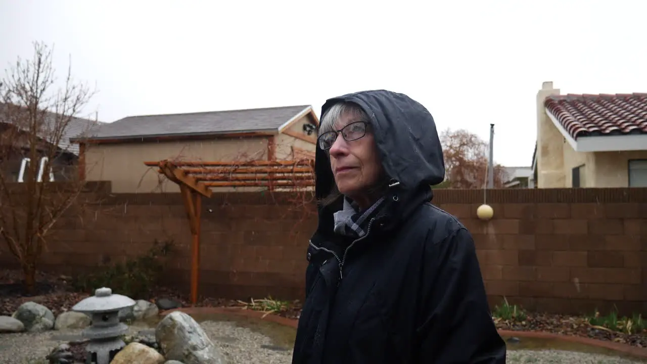 A beautiful old woman wearing a raincoat and hood standing in the rain looking up at the sky smiling during a storm SLOW MOTION