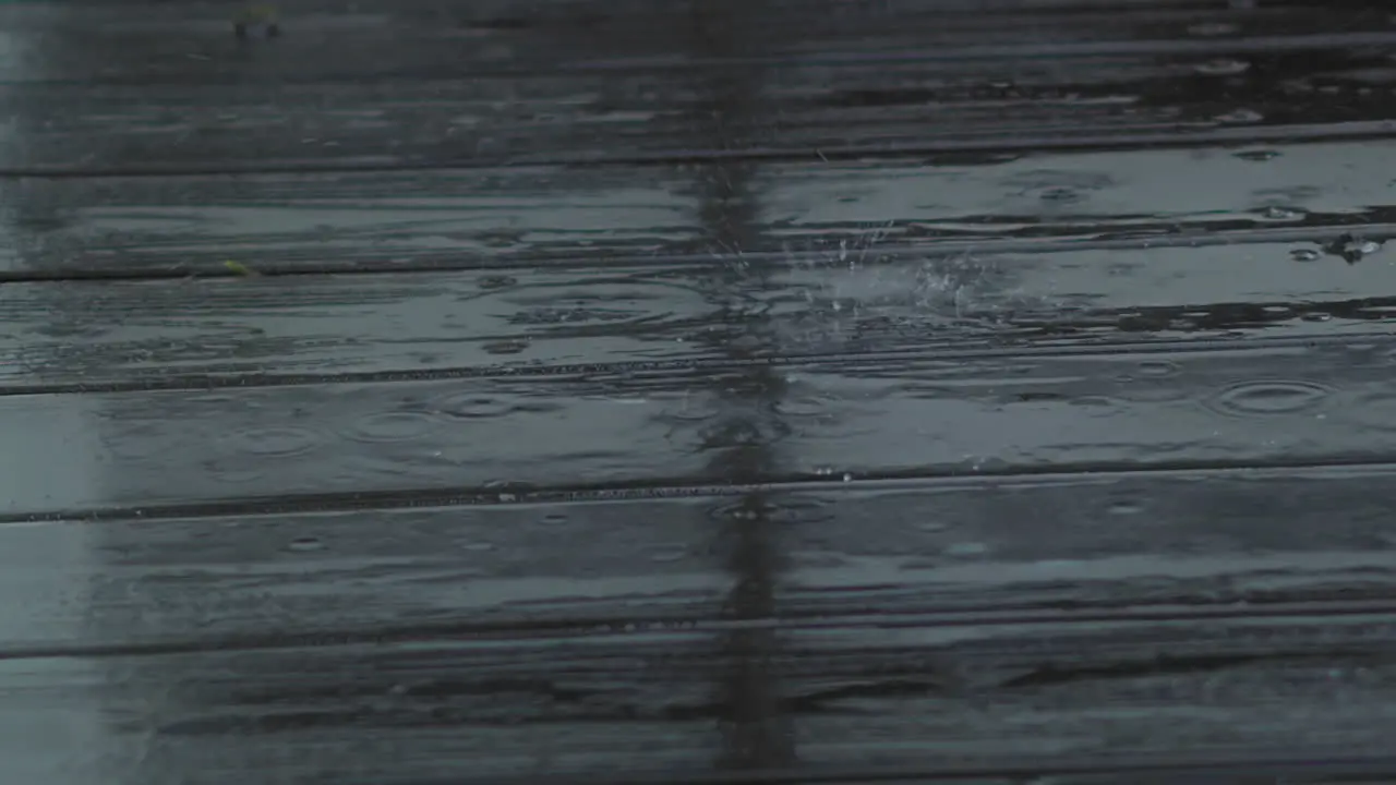 Rain drops fall and splatter on wooden deck close up