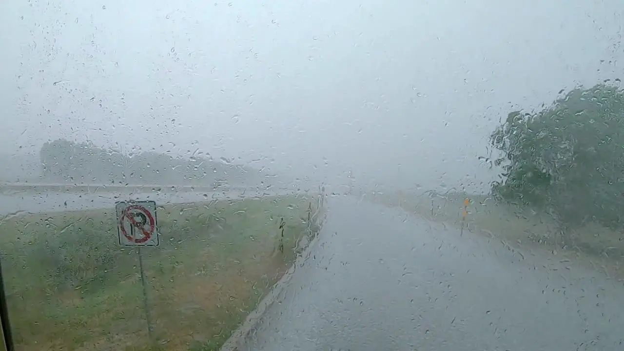 Driving rain hitting a large windshield while vehicle is waiting out the rain storm at a rest area along the interstate