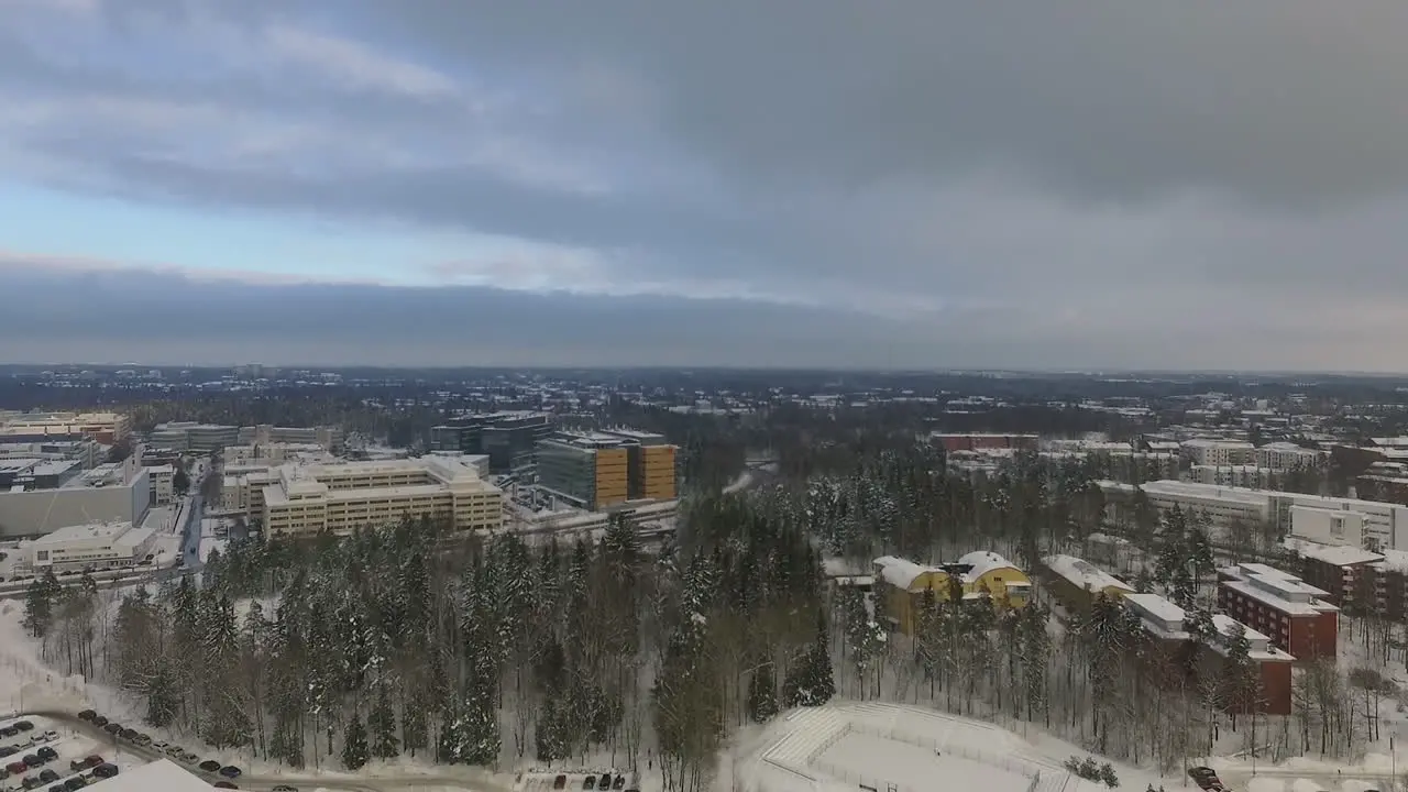 An aerial drone shot that slowly pulls back to reveal views of a densely populated urban city covered in sparkling white snow during winter