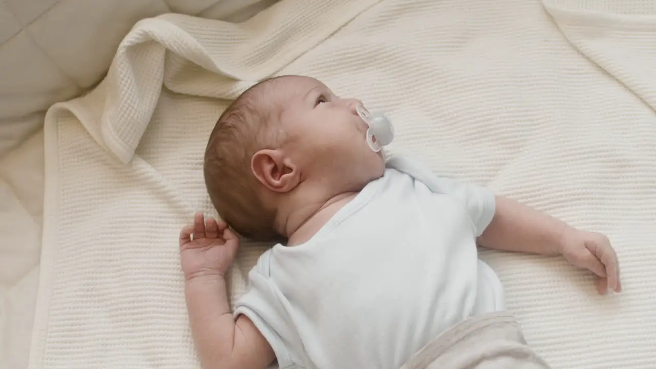 Adorable Newborn Baby Lying On Bed With Dummy In His Mouth