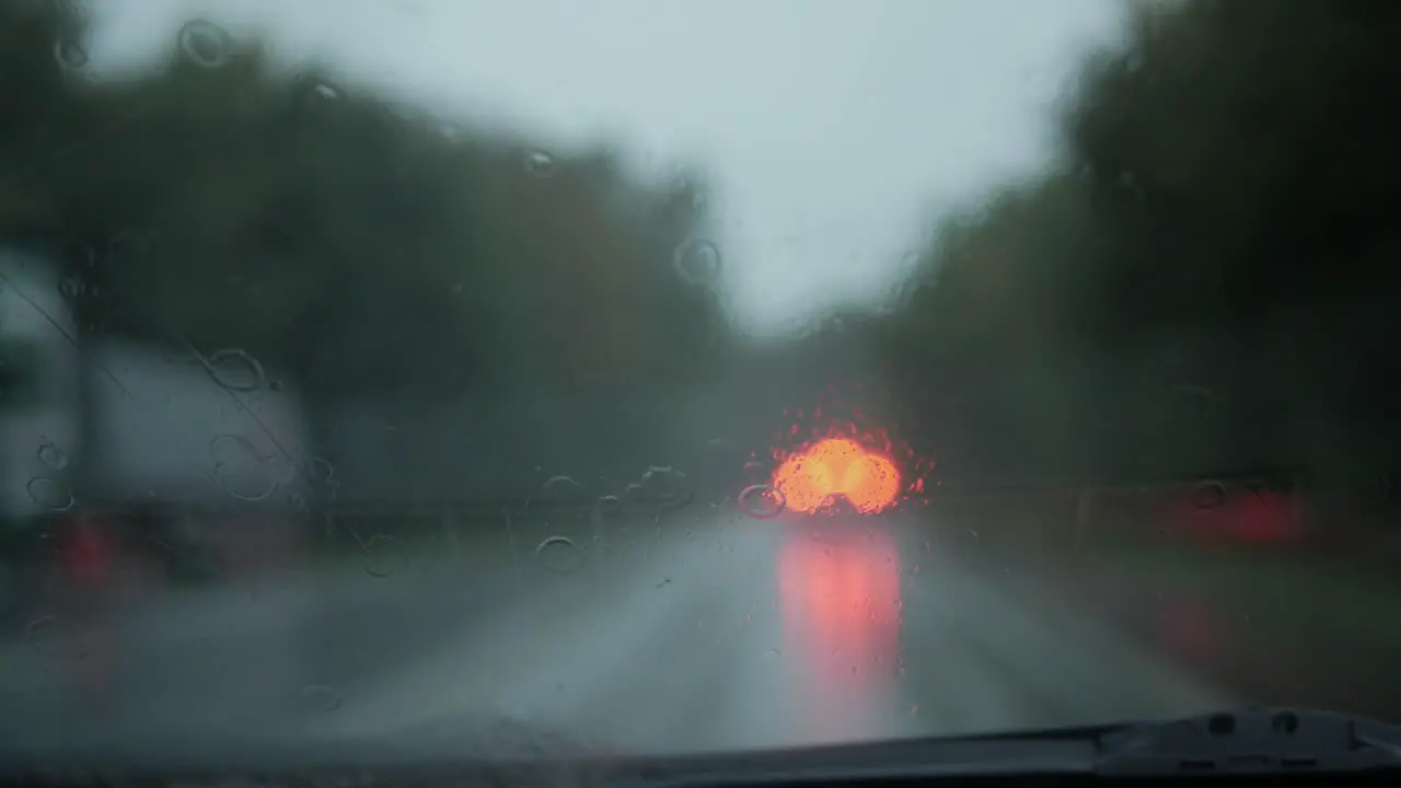 View of the road through wet car window in rain in the evening