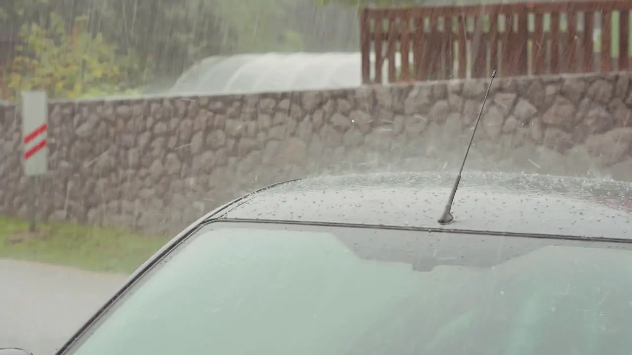 Heavy rain and hail storm over vehicle roof and street weather event at village street