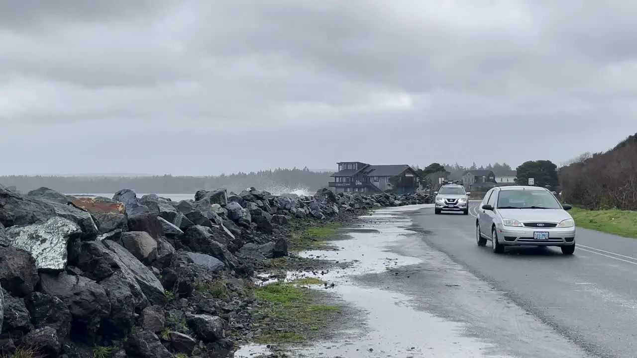 Cars travel on beach road with water splashing over the rocks during strong storm