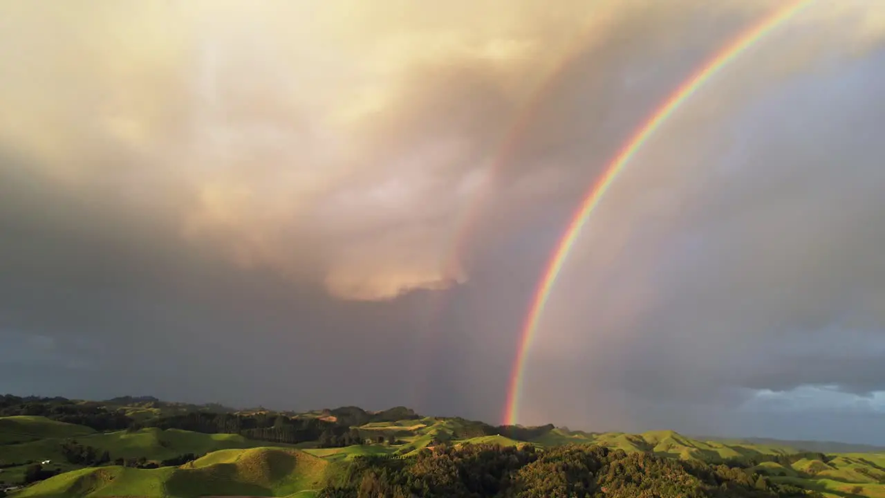 Double rainbow in dark sky over green hills in New Zealand