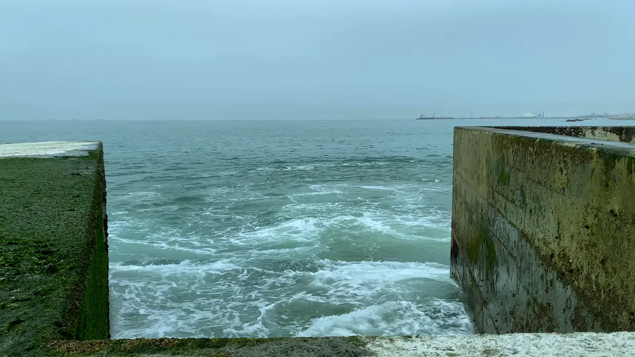 A stormy ocean water slams against a concrete breakwater Pontão da Barra do Douro Molhe Norte Porto Portugal slowmotion