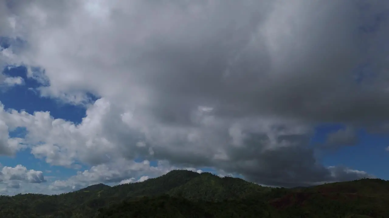 Dense clouds moving over the forested hills during the day covering blue sky