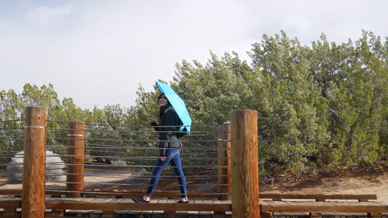 A beautiful young woman with blue weather umbrella walking across a bridge during a rain storm in the desert SLOW MOTION