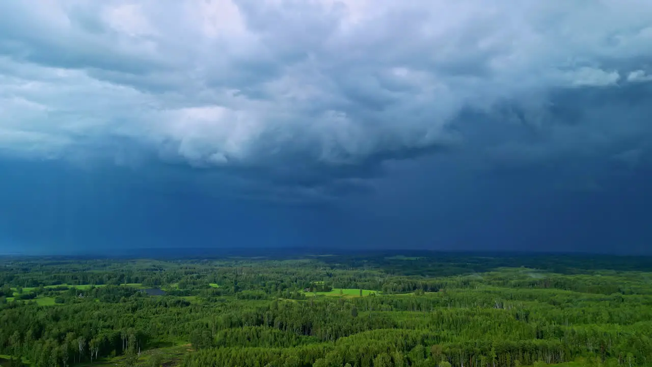 Dark rain storm clouds flowing above woodland landscape aerial drone view