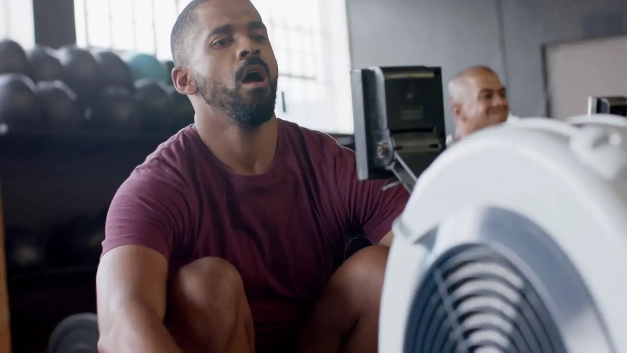 Determined biracial man training hard on rowing machine at gym in slow motion