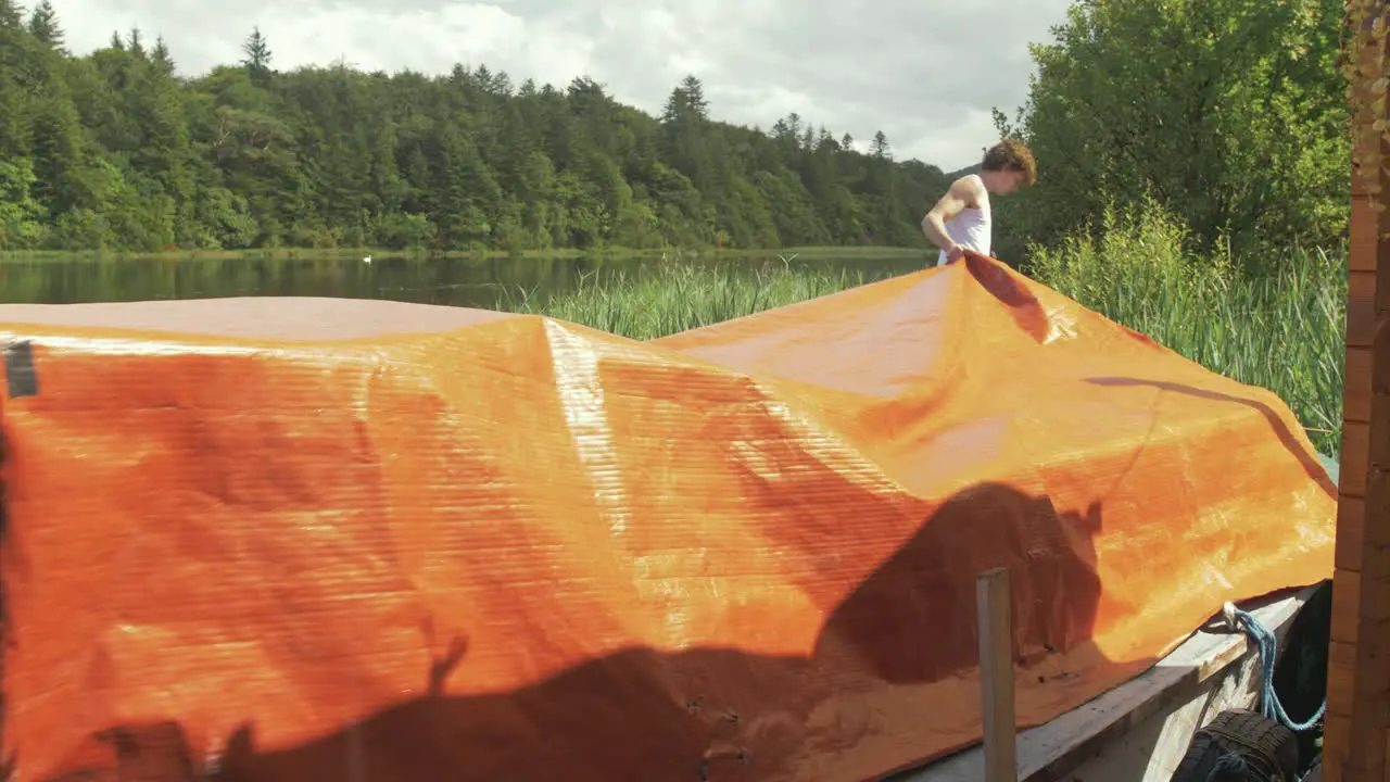 Young man pulling boat cover over old wooden motor boat