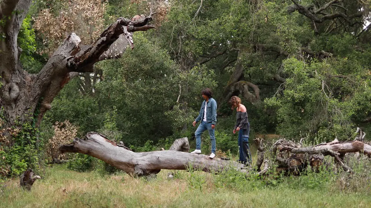 A Hispanic couple walks on a fallen tree branch in a park laughing and enjoying each others company