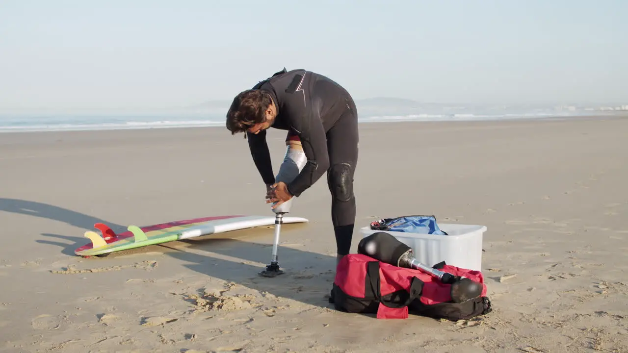 Male Surfer With Disability Taping Artificial Leg On The Coast