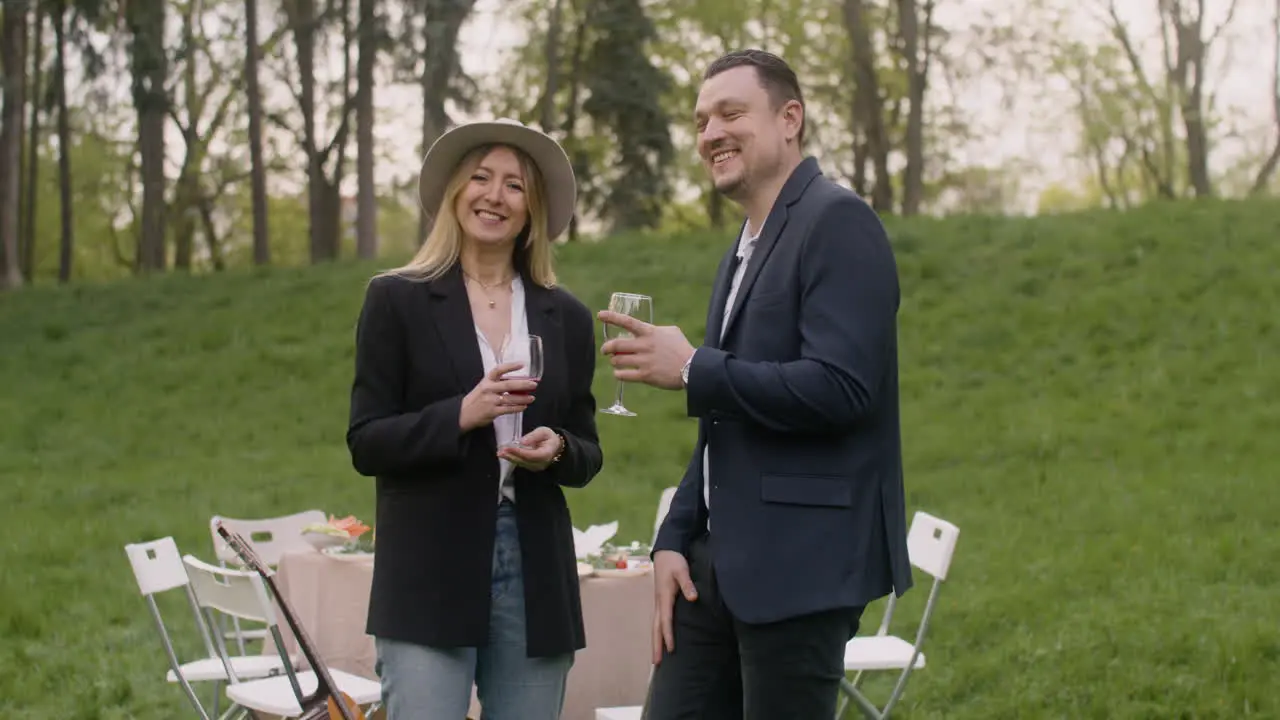 Middle Aged Man And Woman Laughing And Looking At Camera While Holding Wine Glasses In The Park