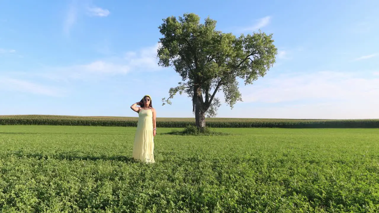 girl with a lovely dress standing outdoors on a grass land with a lonely three