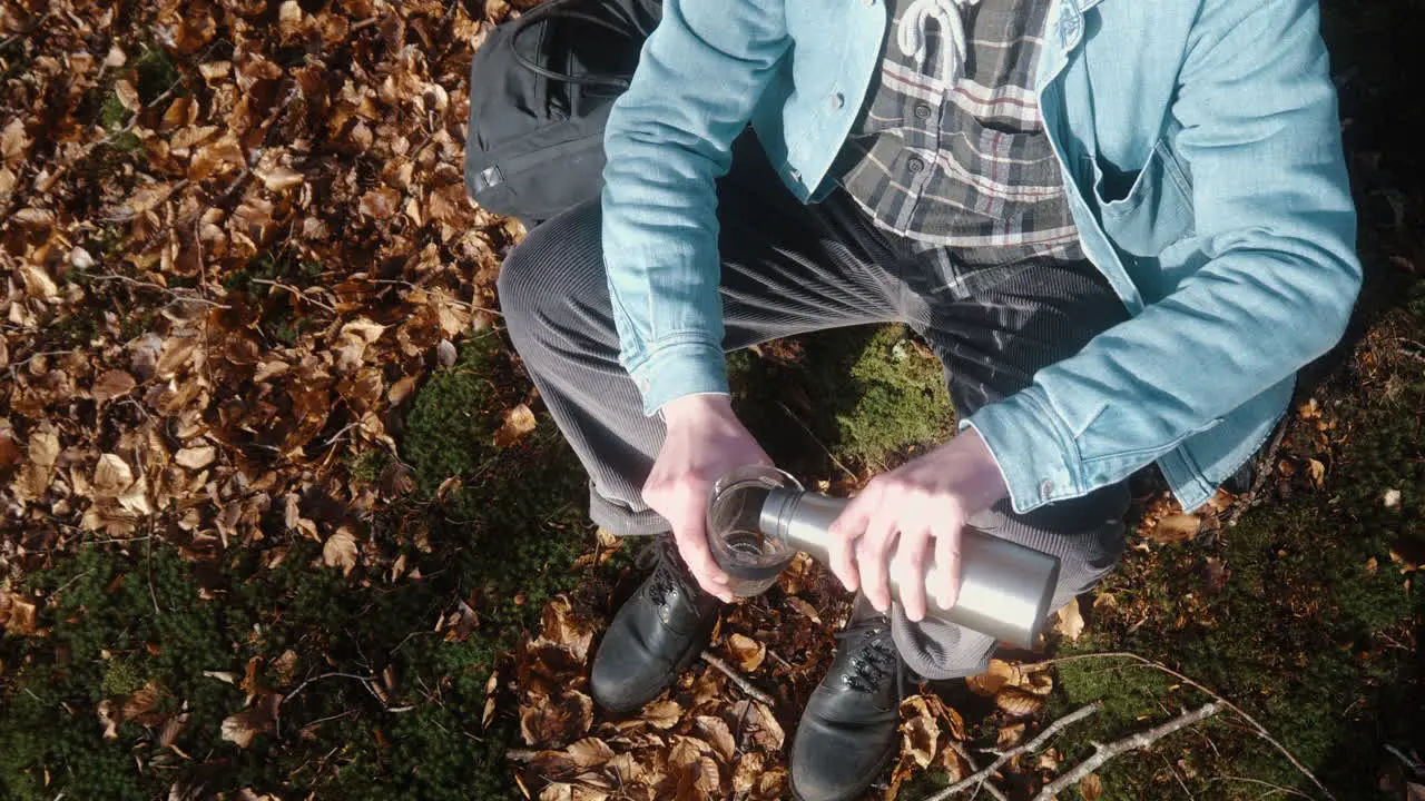 man sitting down on the forest floor pouring coffee in his cup on a sunny autumn day