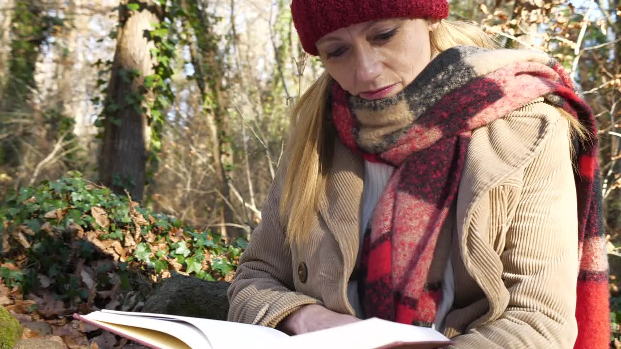 Closeup Circling Woman in winter clothes sits reading book in forest