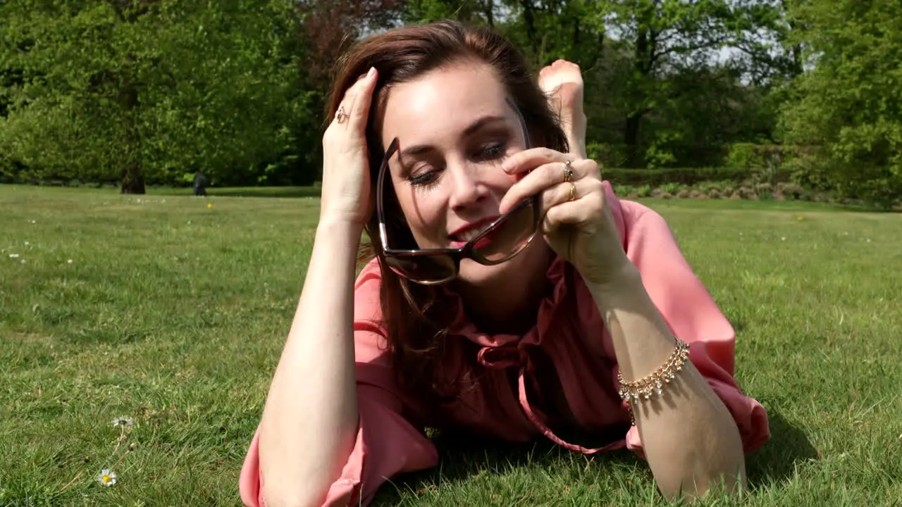 Attractive adult woman rolling playful in the grass en putting on sunglasses