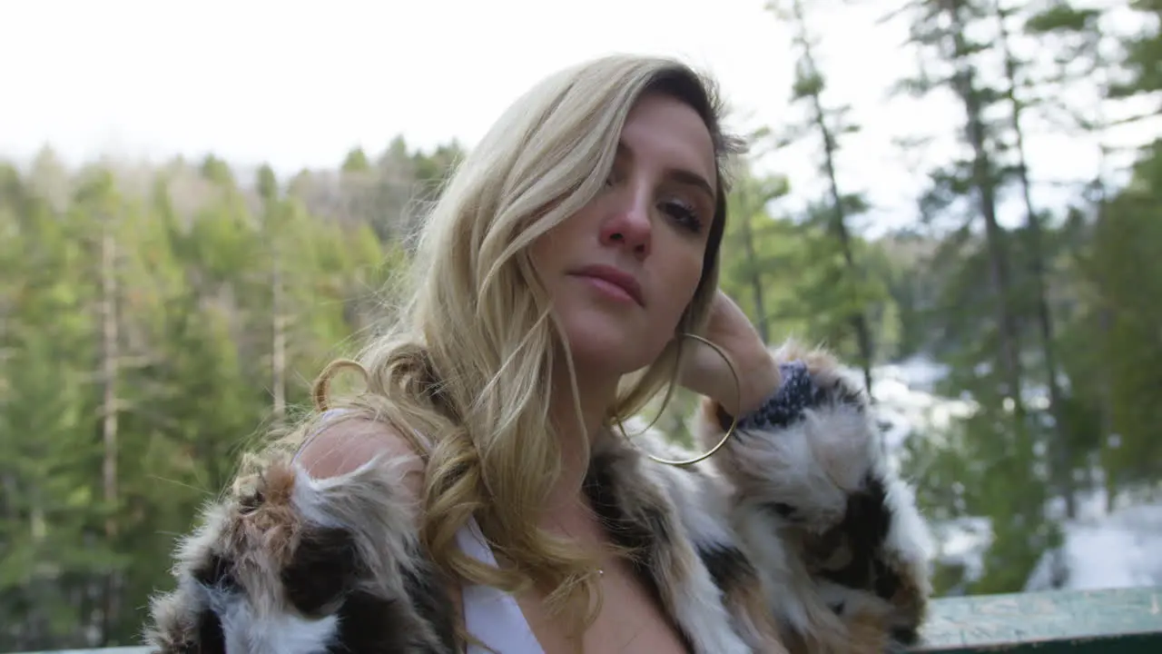 Confident young blonde woman posing on an overlook scenic winter forest in the background