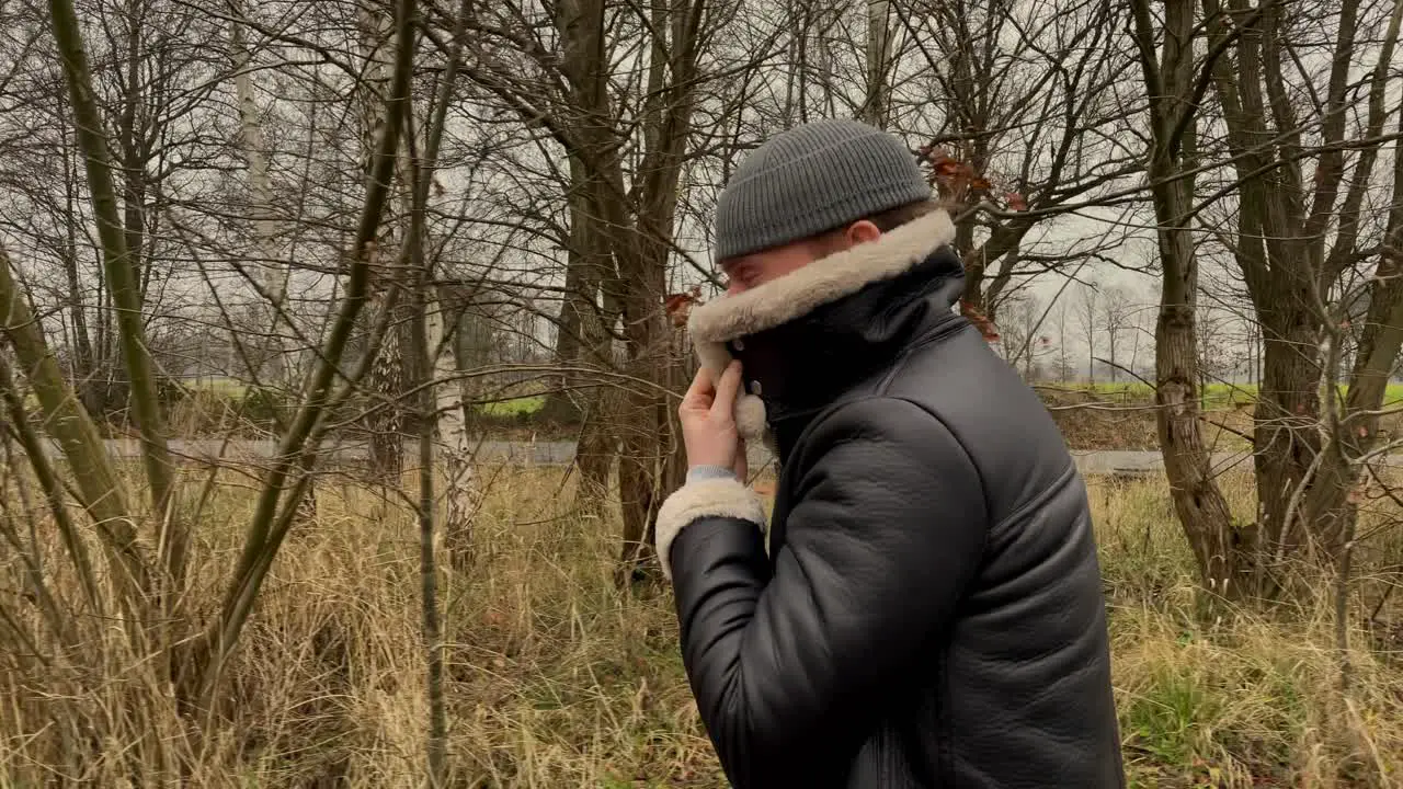 Slow motion track shot of young fashionable man with hat and leather jacket walking outdoors in nature