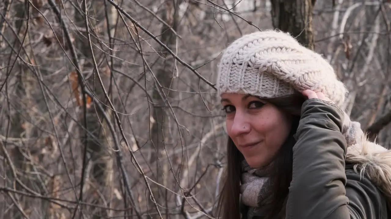 Beautiful Woman Wearing Winter Clothes In The Forest Looks And Smiles At The Camera While Touching Her Hair medium shot slow motion